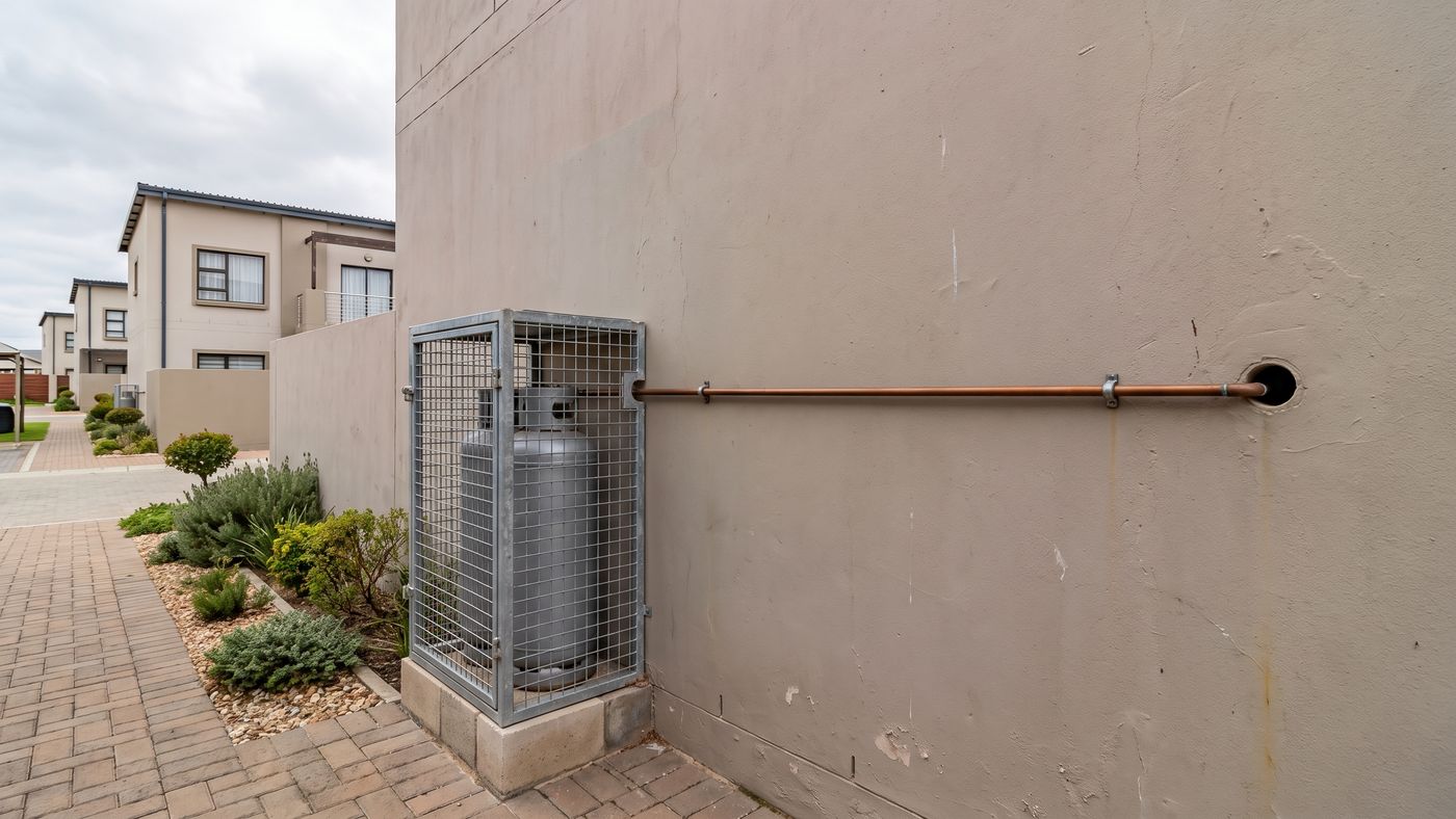 Caged gas cylinder against a blank side wall of a townhouse in a security complex